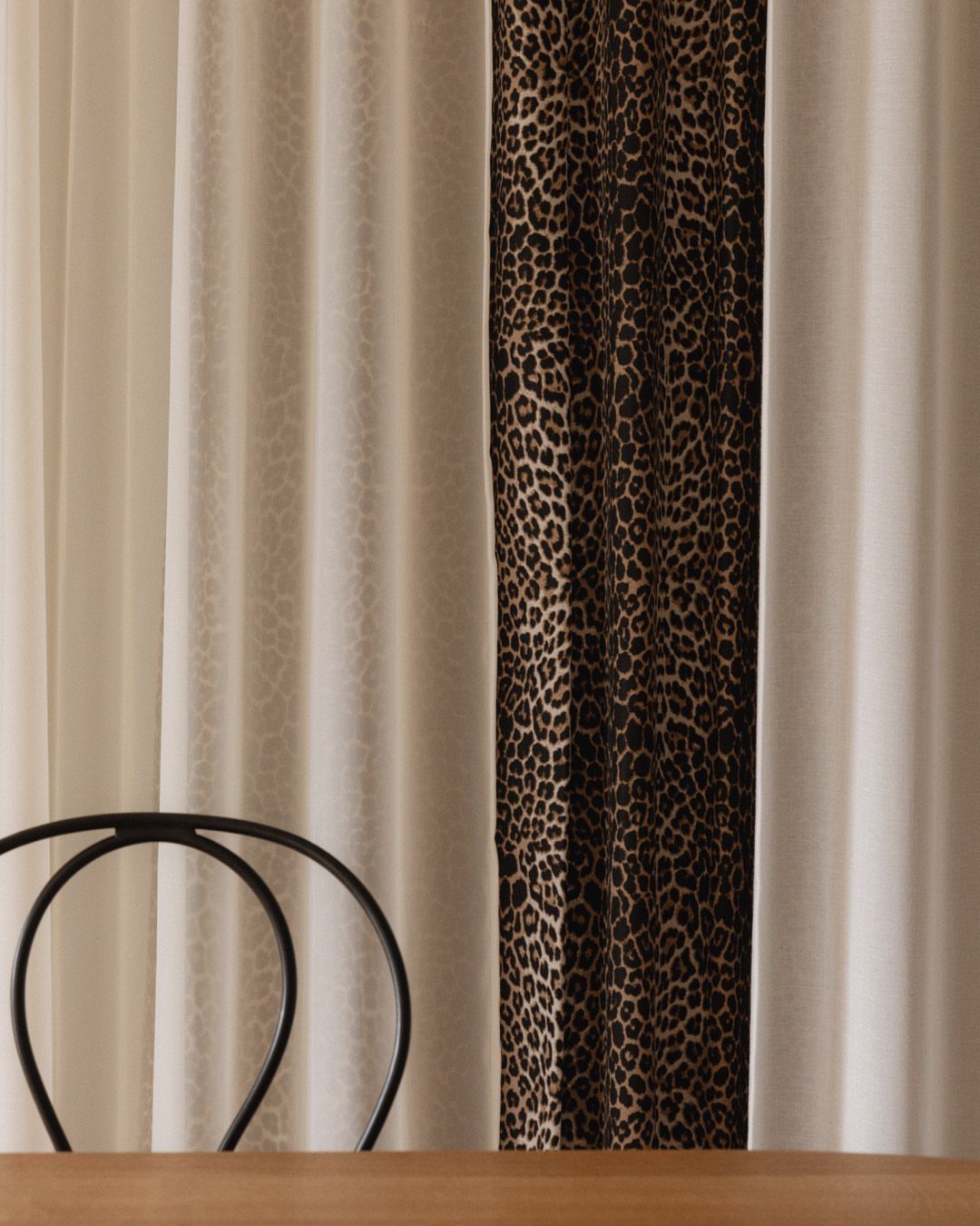 Leopard print curtain panel between white sheer curtains with a black chair foreground.