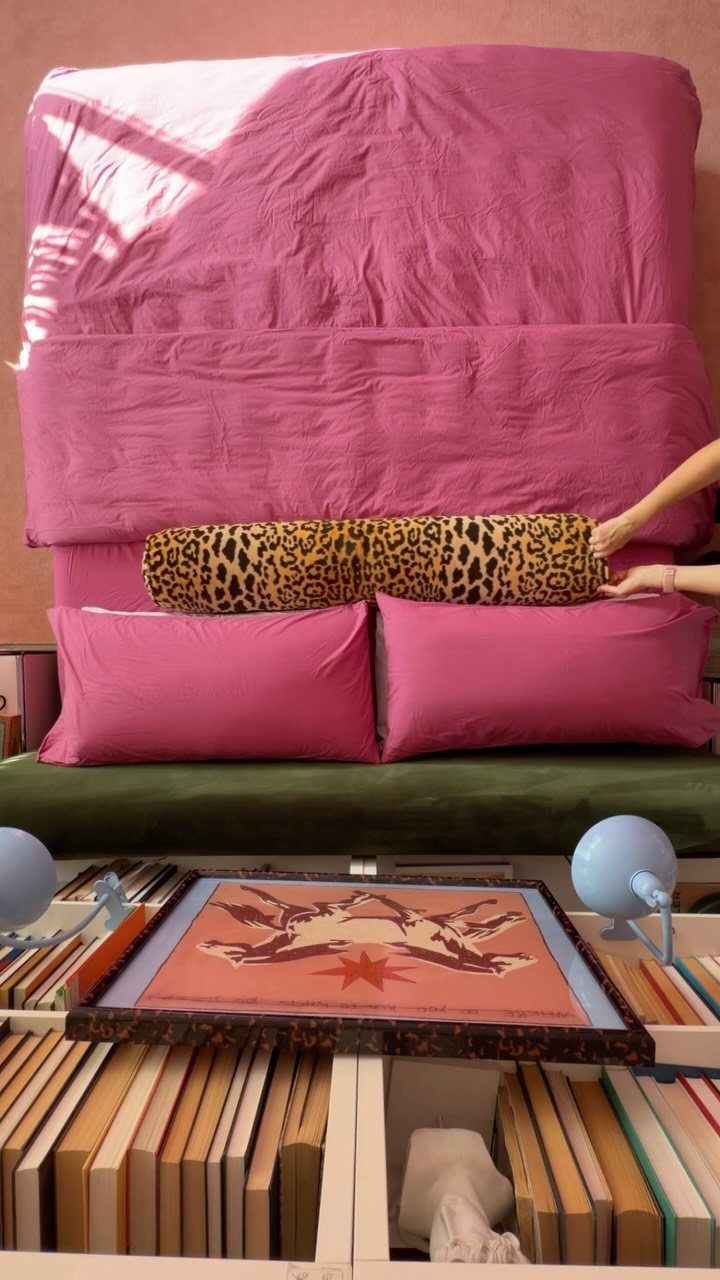 Leopard print bolster pillow on a bed with bright pink bedding and pillows.