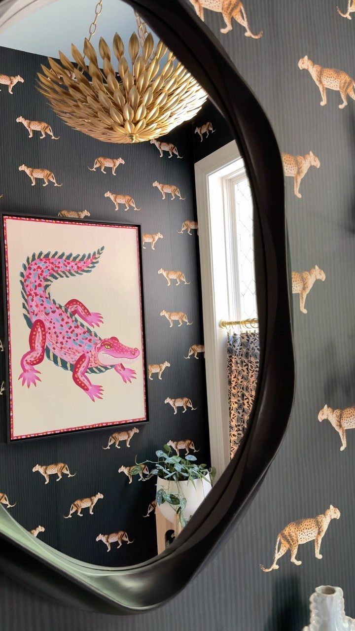 Leopard print curtains and leopard pattern wallpaper reflected in an oval black mirror.