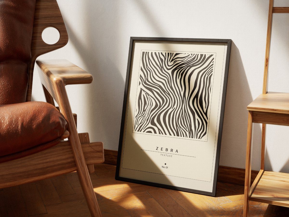 Framed zebra print art leaning against a white wall next to a leather chair.