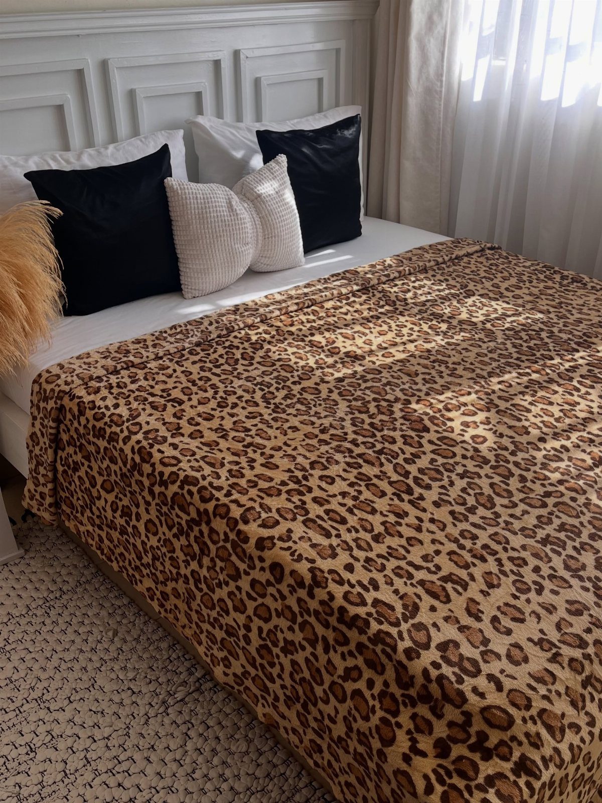 Leopard print blanket covering a bed with black and white accent pillows.