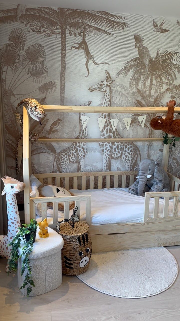 Jungle animals wallpaper in a nursery with a house-shaped wooden bed and plushies.