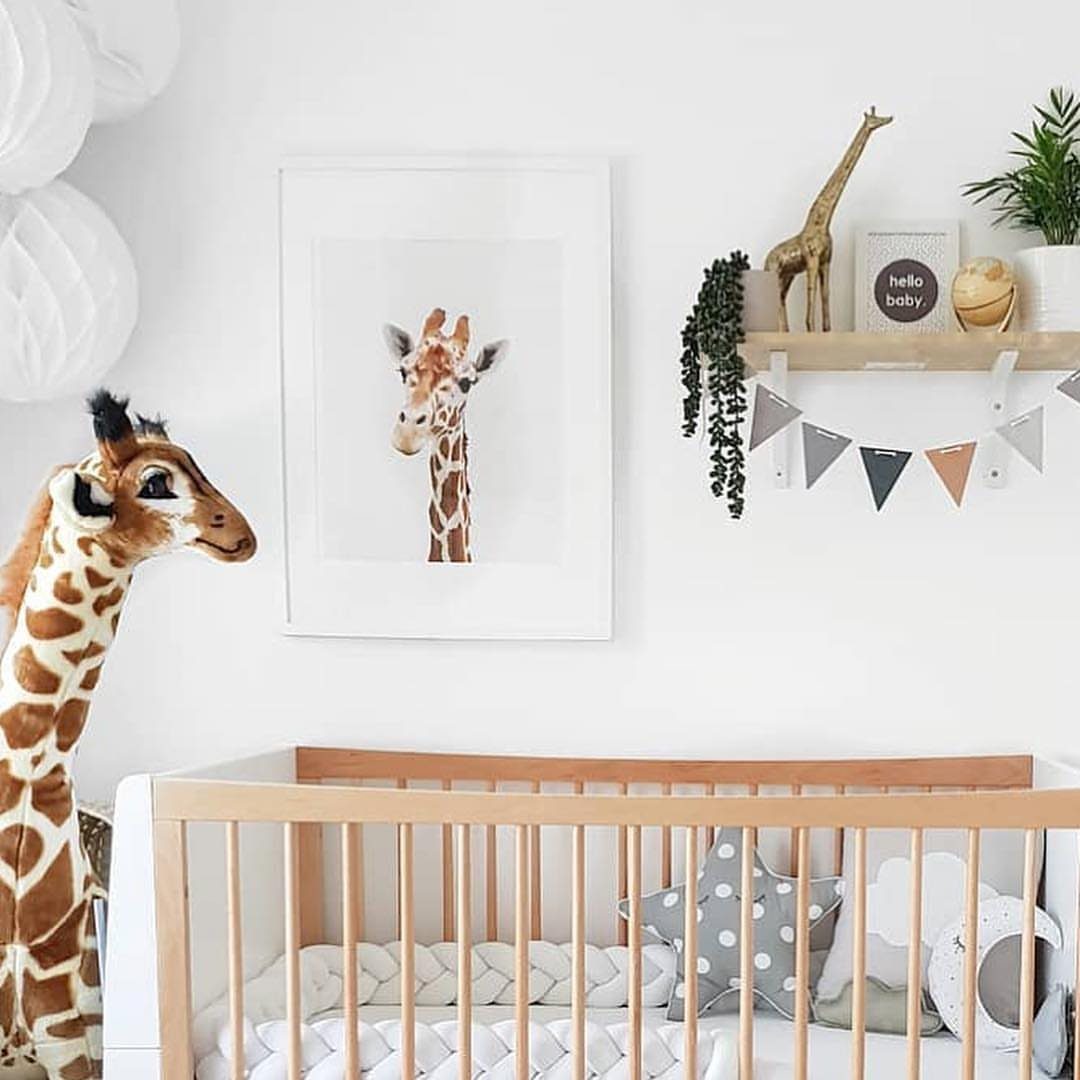 Large plush giraffe standing next to a wooden baby crib in a nursery