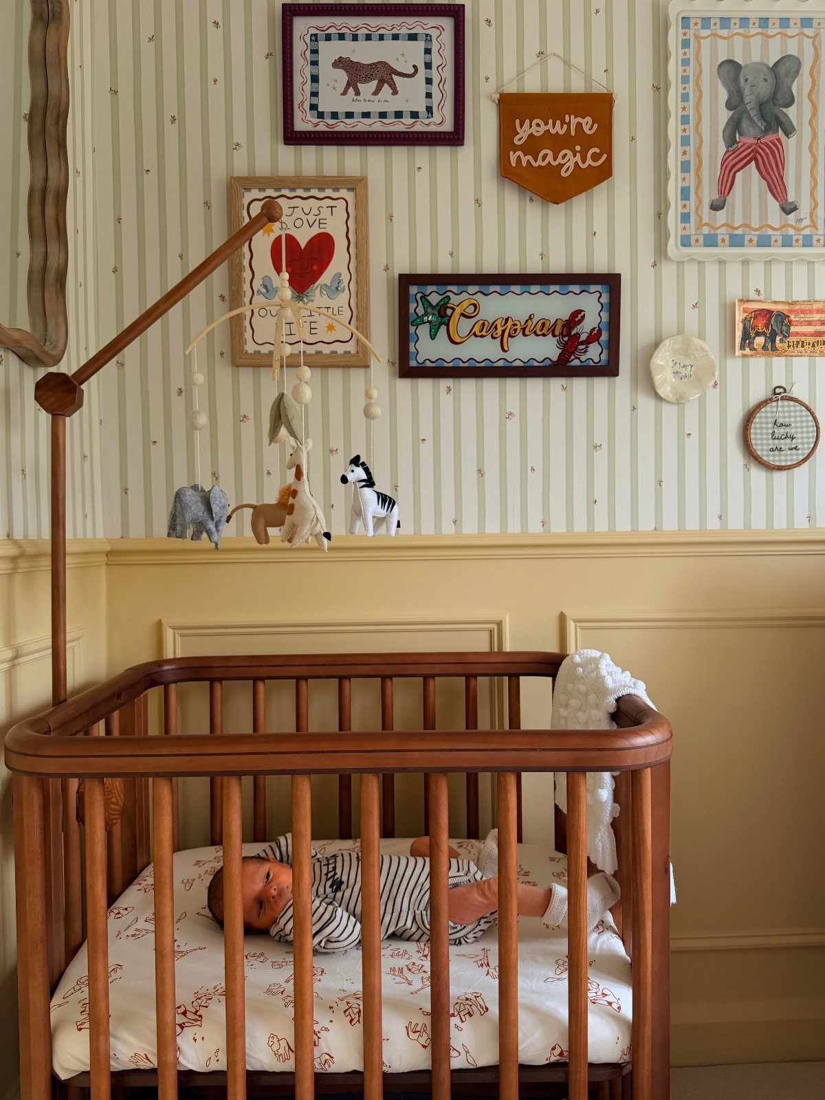 Baby in wooden crib with safari animal sketches and decor on striped walls