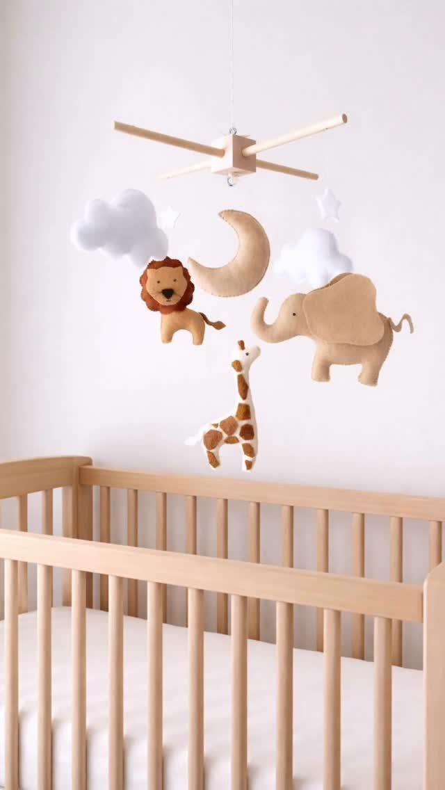 Baby animal mobile with lion, elephant, and giraffe hanging over a wooden crib