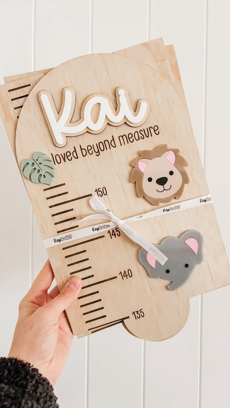 Wooden growth chart with animal illustrations and the name Kai held by a hand.