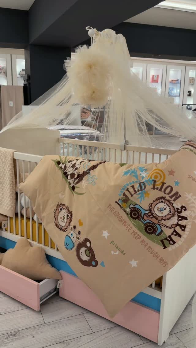 White baby crib with a safari animal themed blanket and white tulle canopy.