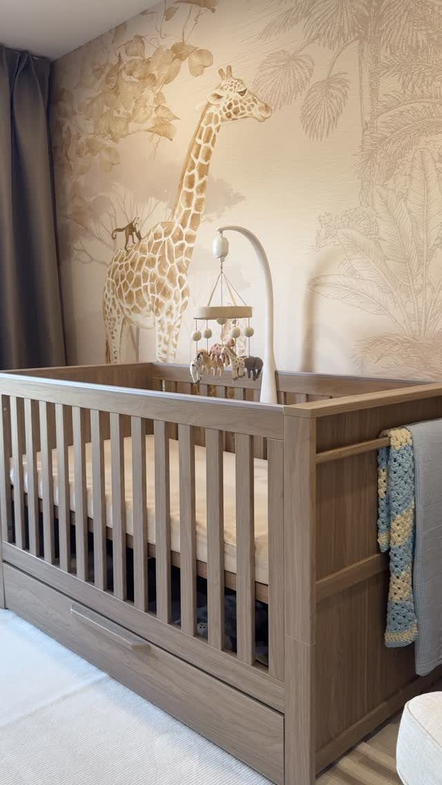 Wooden baby crib in front of a beige giraffe and jungle wall mural.