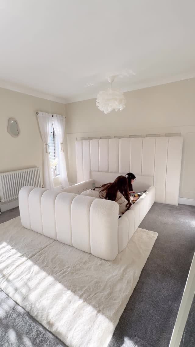 White vertically channeled tufted fabric wall panel behind a matching upholstered bed frame.