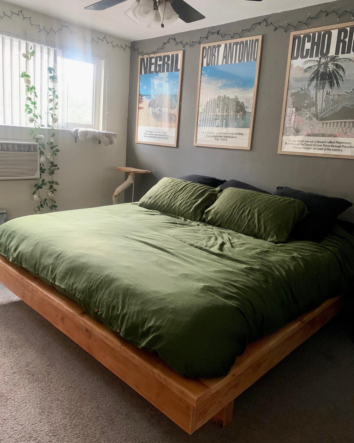 Bed with olive green linens and wooden frame against grey wall with posters