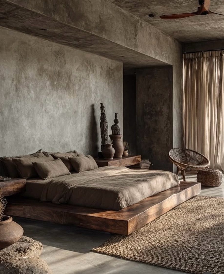 Low wooden platform bed with brown linens against a grey concrete wall
