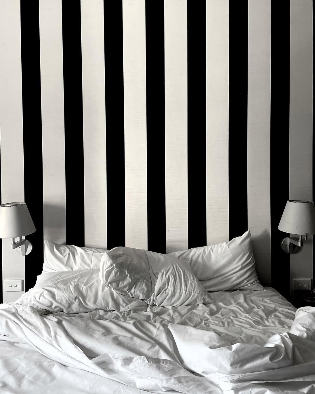 Bed with white linens against a bold black and white striped statement wall.