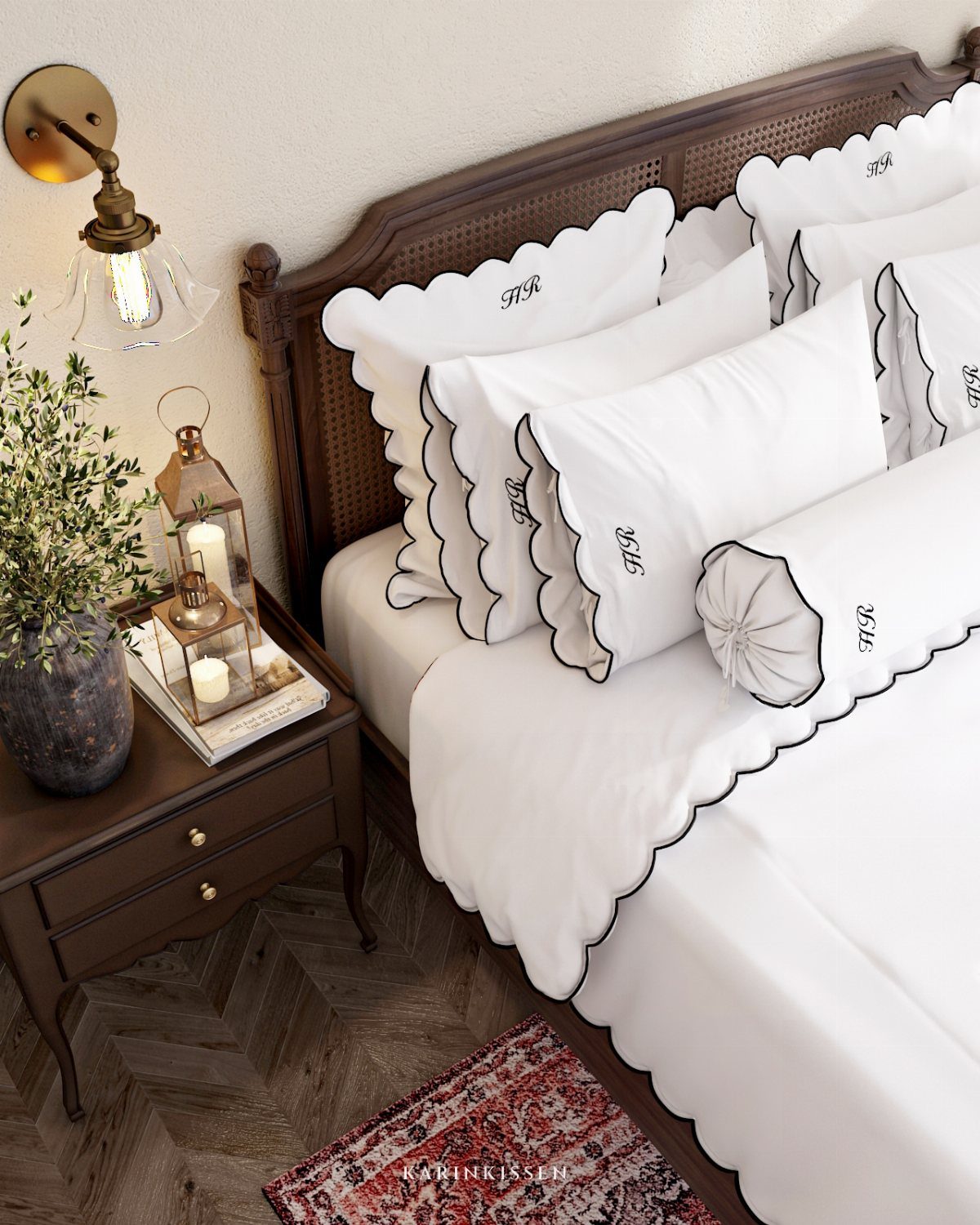 White scalloped bedding on a bed with a dark wood headboard and nightstand.