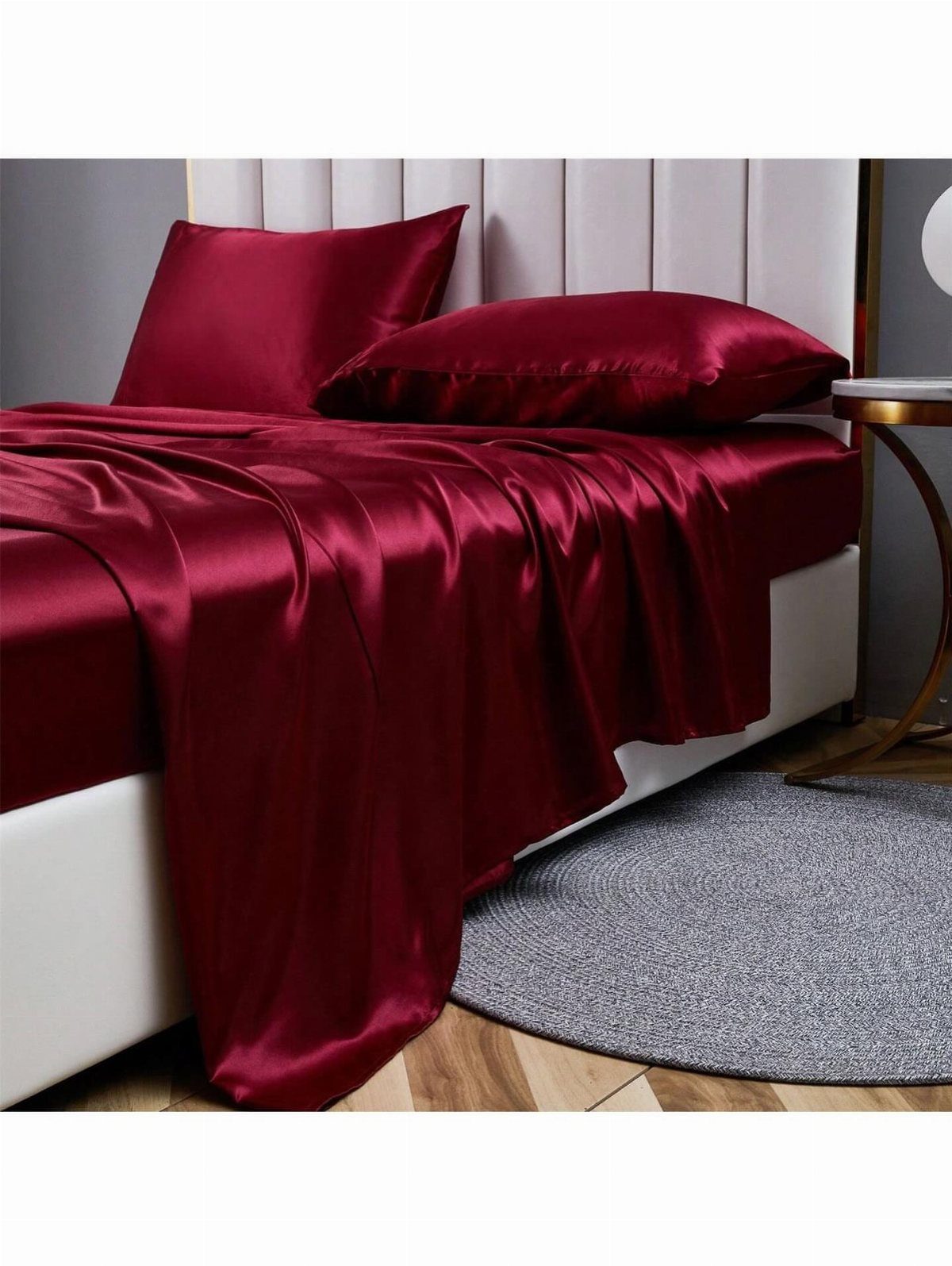 Deep red satin bedding and pillows on a white bed with grey rug.