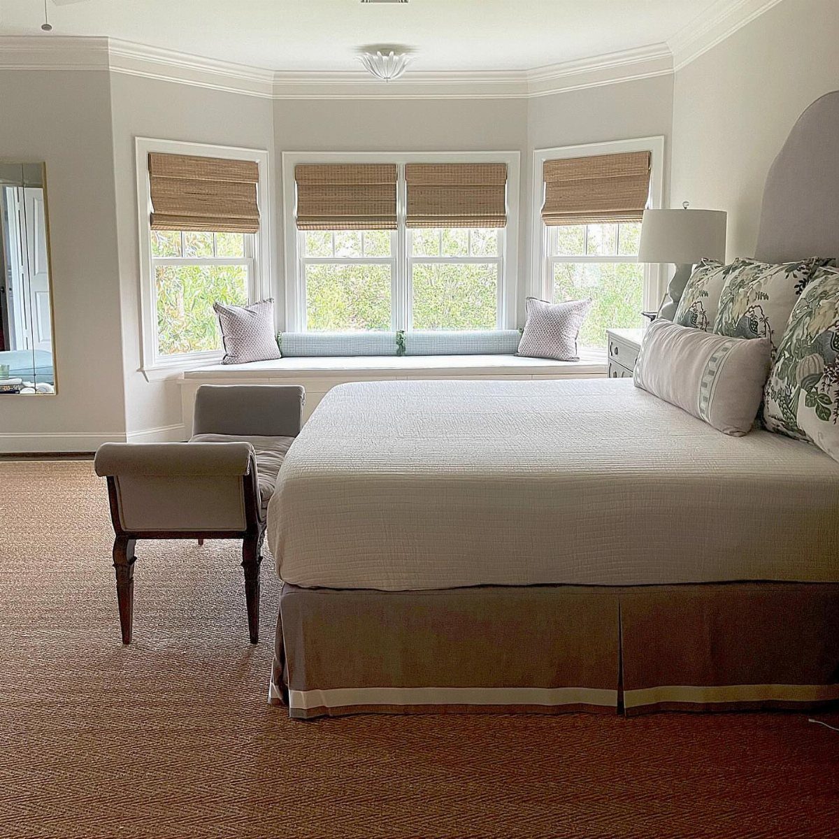 Bedroom with white bedding, grey upholstered bench, and a window seat with cushions.