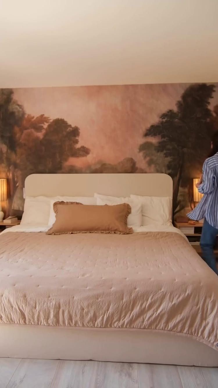 Bedroom with a landscape mural of trees and sunset behind a beige bed.