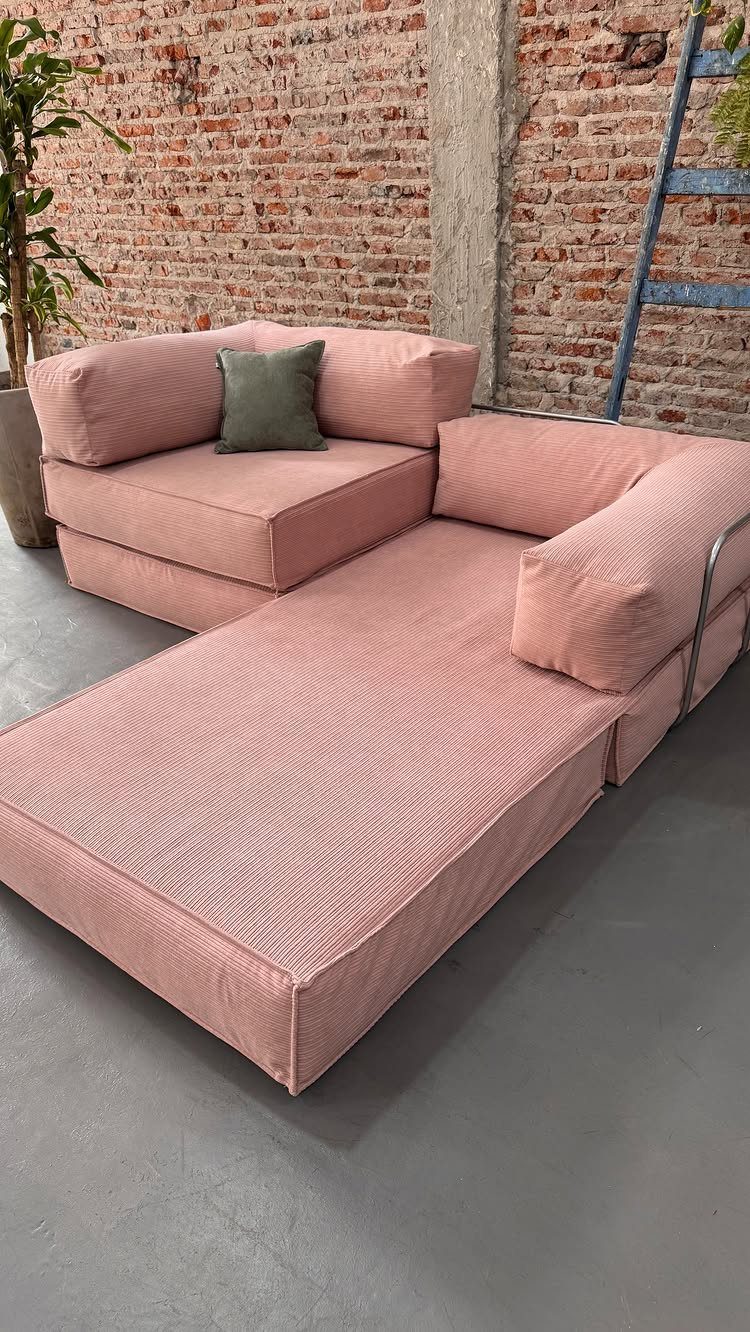 Pink modular sectional sofa with a chaise lounge against a red brick wall.