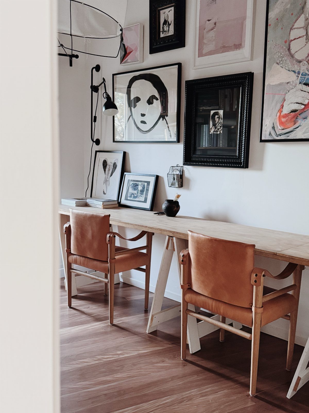 Long wooden desk with two brown leather chairs and framed art on wall
