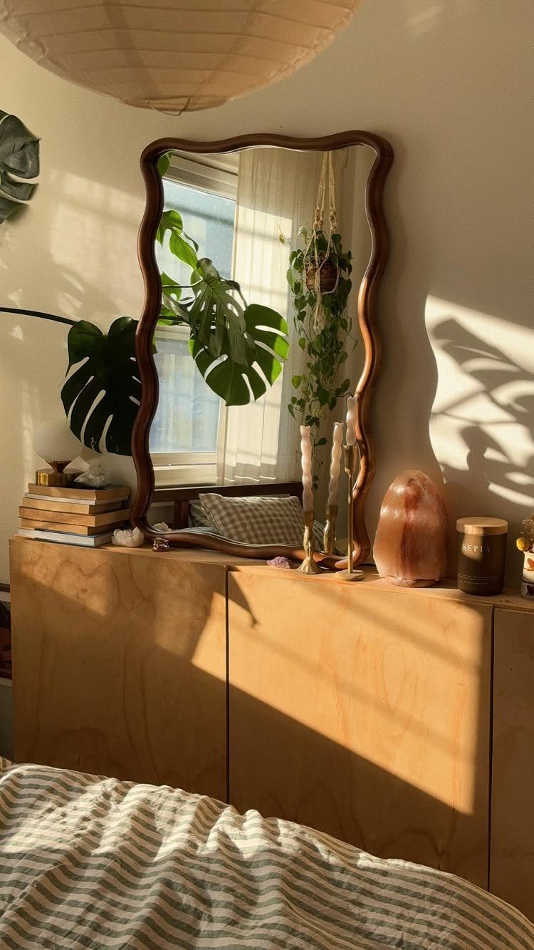 Wavy brown mirror on a wooden sideboard with plants and a salt lamp.
