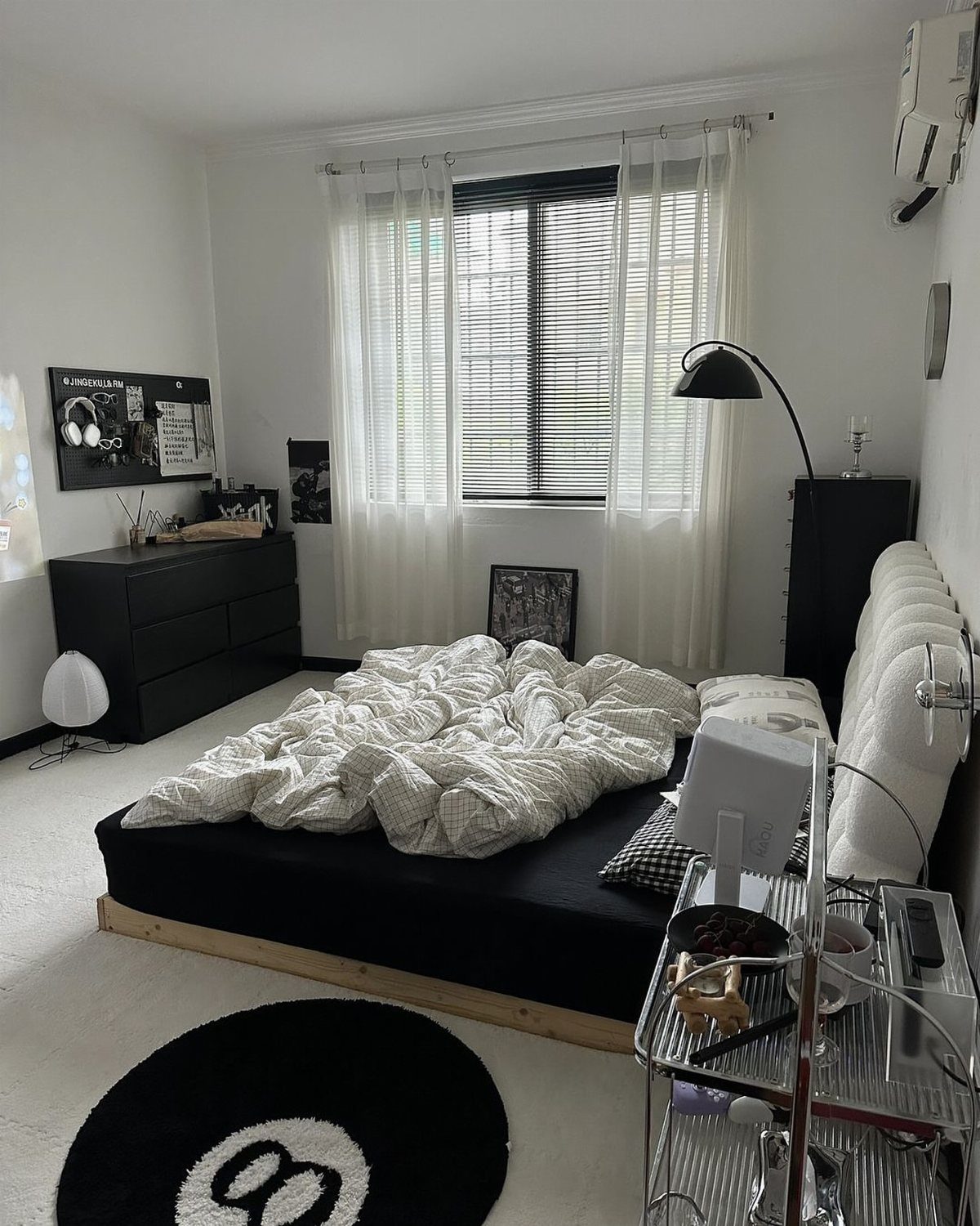 Black and white bedroom with 8-ball rug, black bed, and white curtains.