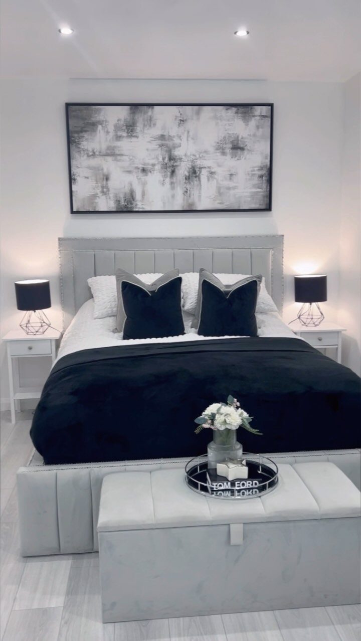 Modern bedroom with black and white decor, grey bed, and abstract wall art.