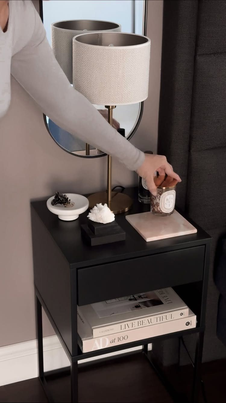 Black bedside table with a white lamp, books, and decorative items in a bedroom.