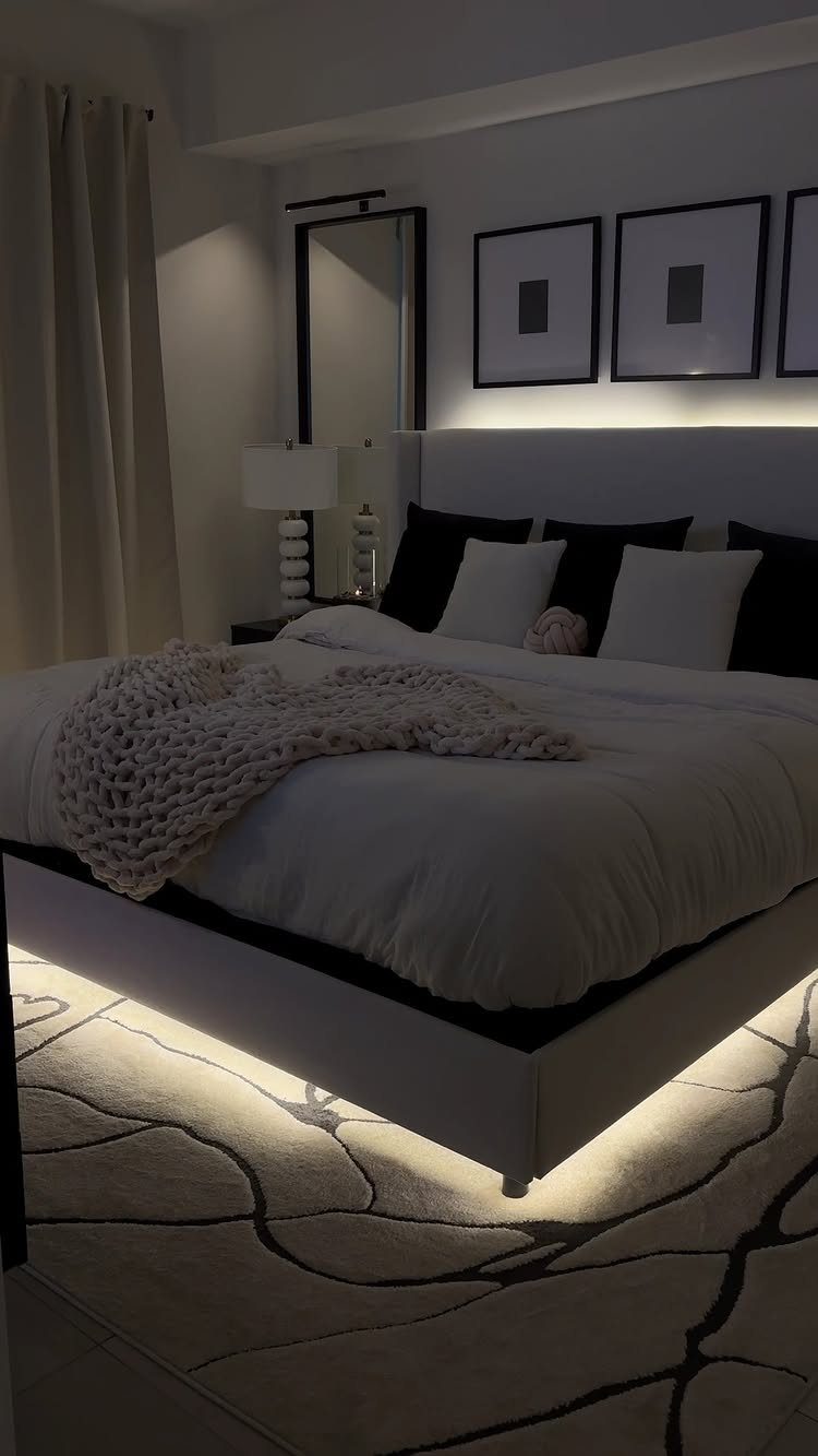 Modern bedroom with black and white bedding, under-bed lighting, and framed wall art.