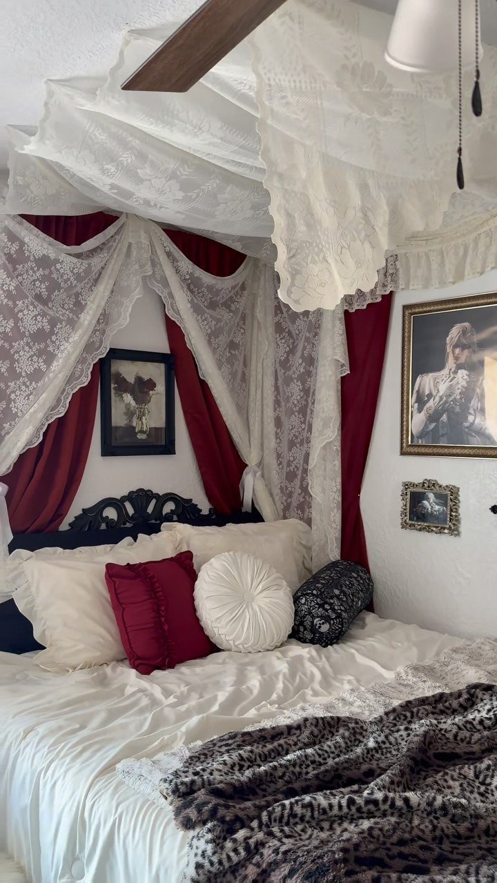 Bed with white lace canopy and red curtains, featuring plush cushions and faux-fur throw.