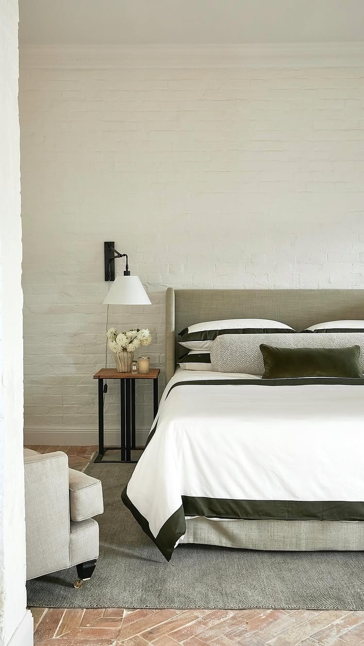 Large bed with white and green linens, neutral headboard, and bedside lamp.