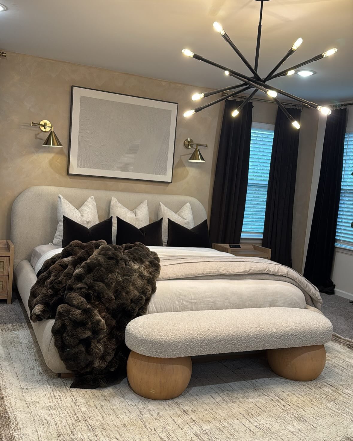 Modern bedroom with a curved beige headboard, faux-fur throw, and spiky black chandelier.