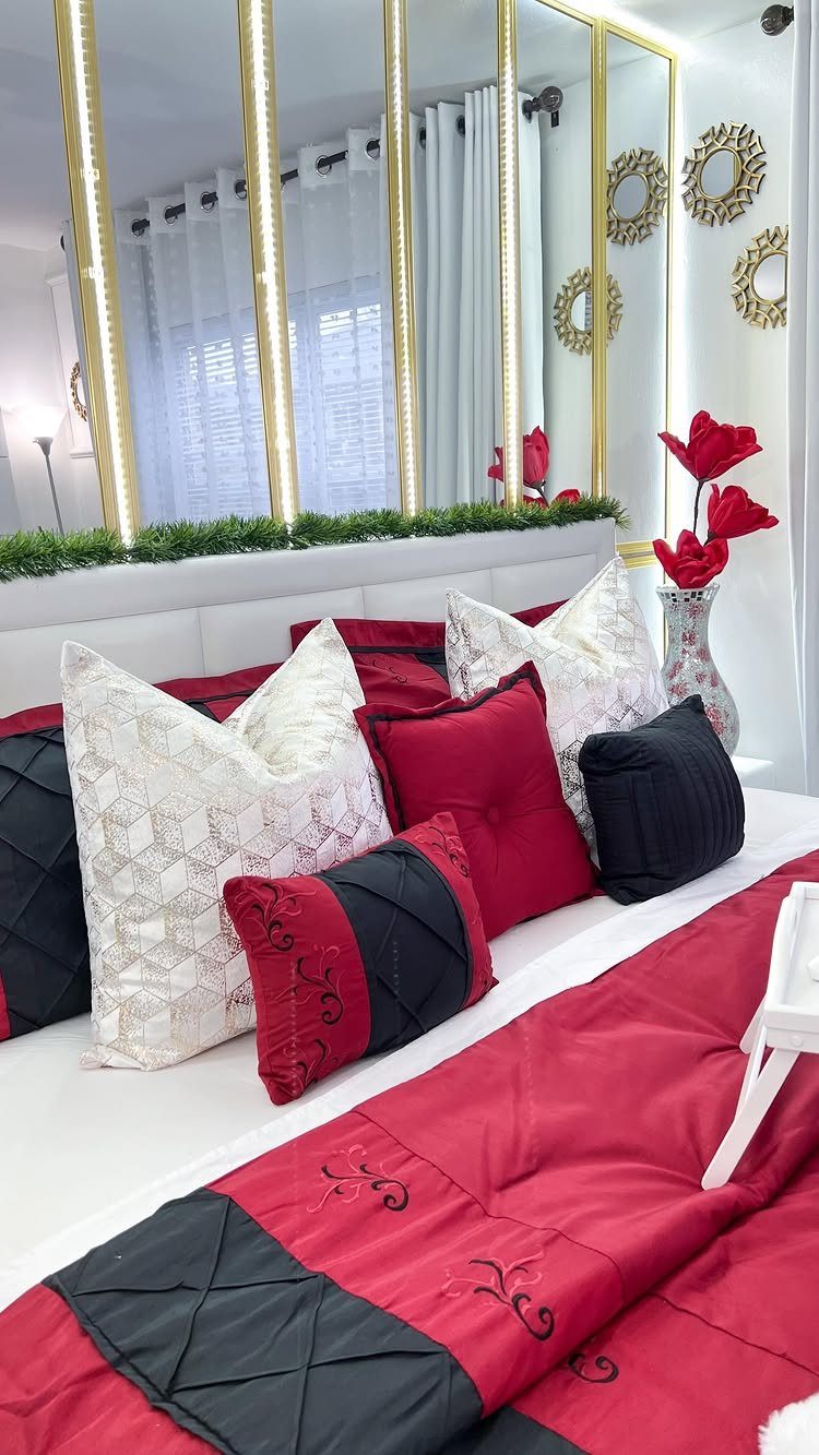 Bed with red and black linens and a large gold-framed mirror behind it.