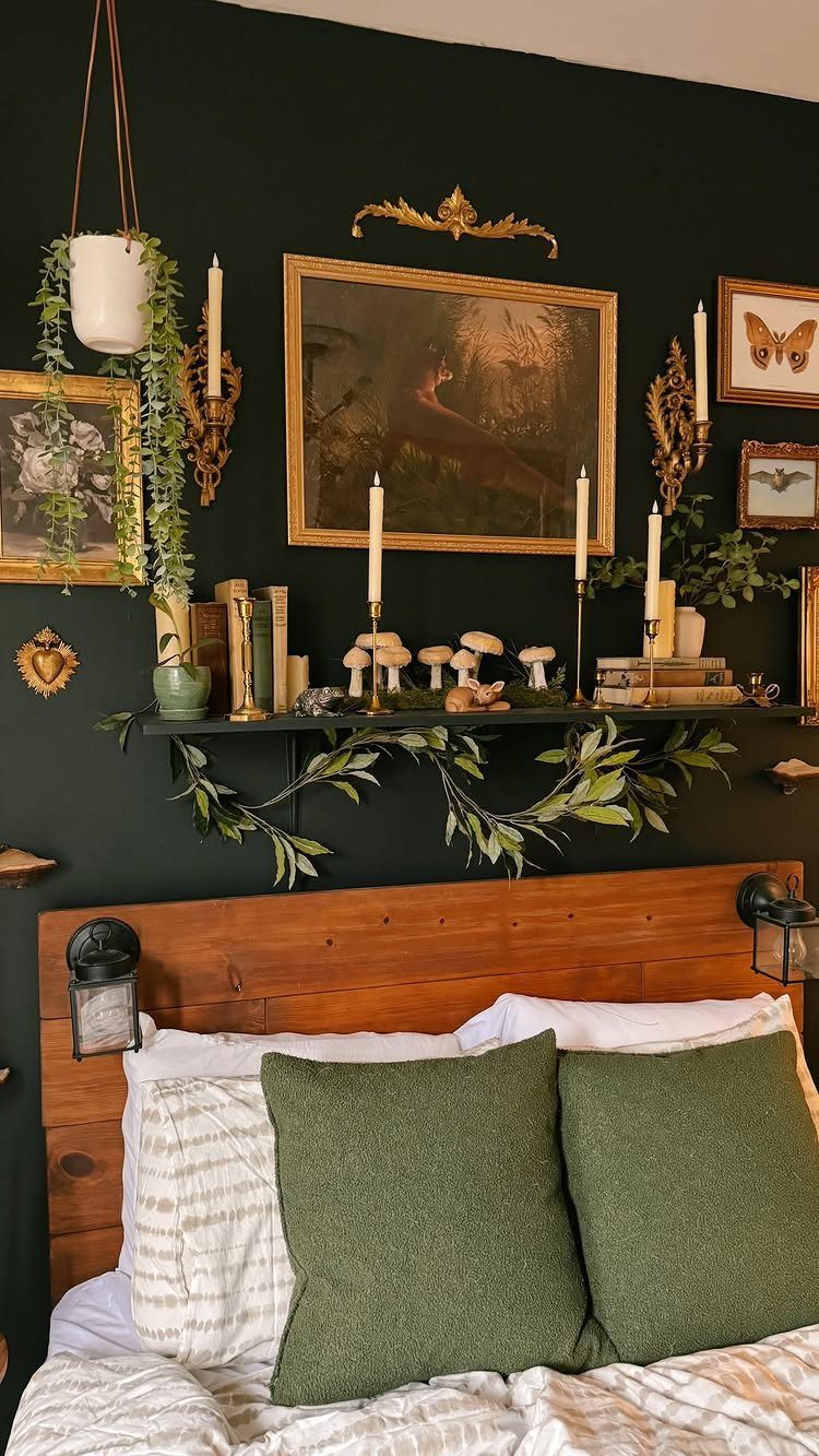 Gold-framed paintings and candles on a dark green wall above a wooden headboard.