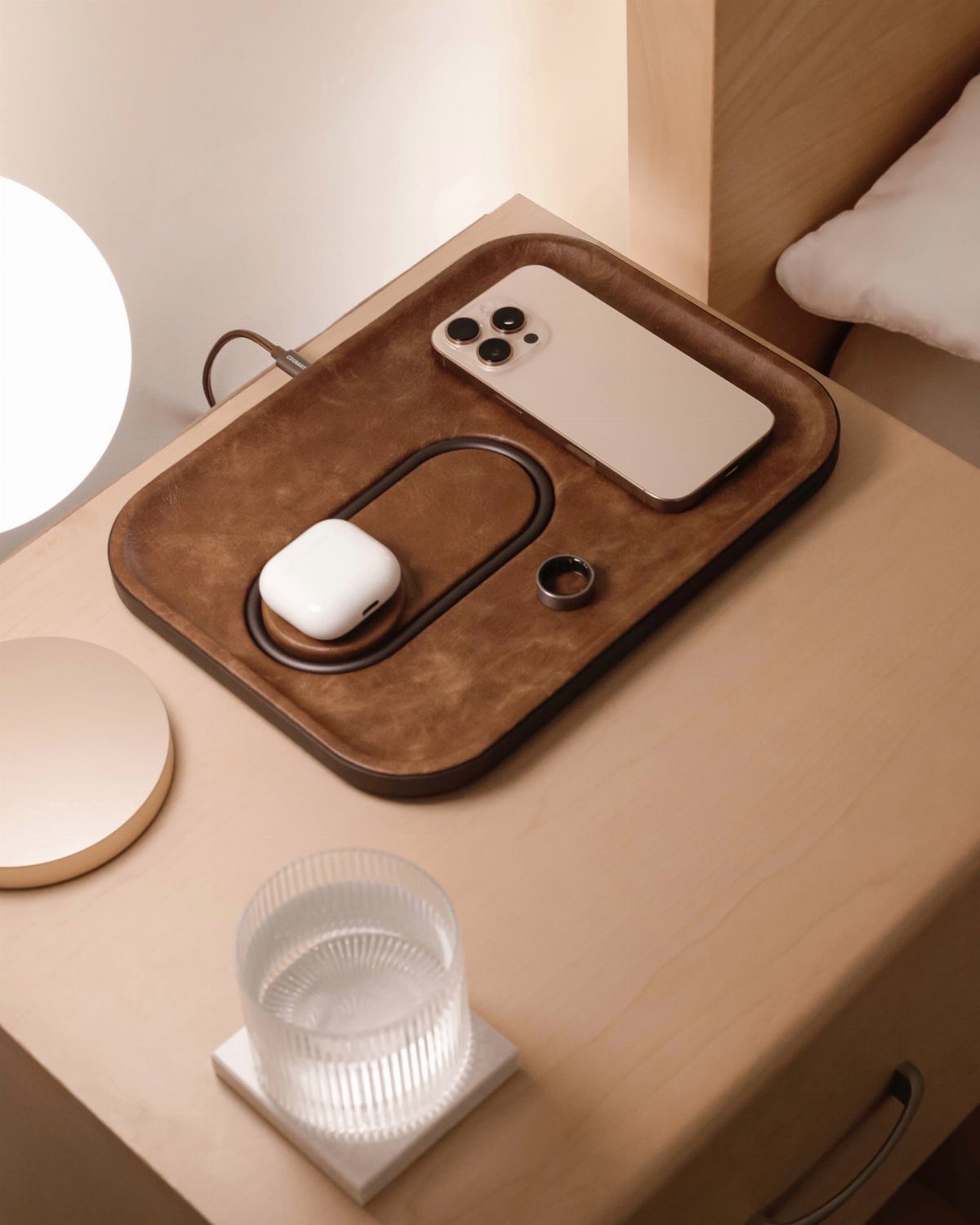 Brown leather valet tray on a nightstand holding a phone and wireless earbuds.