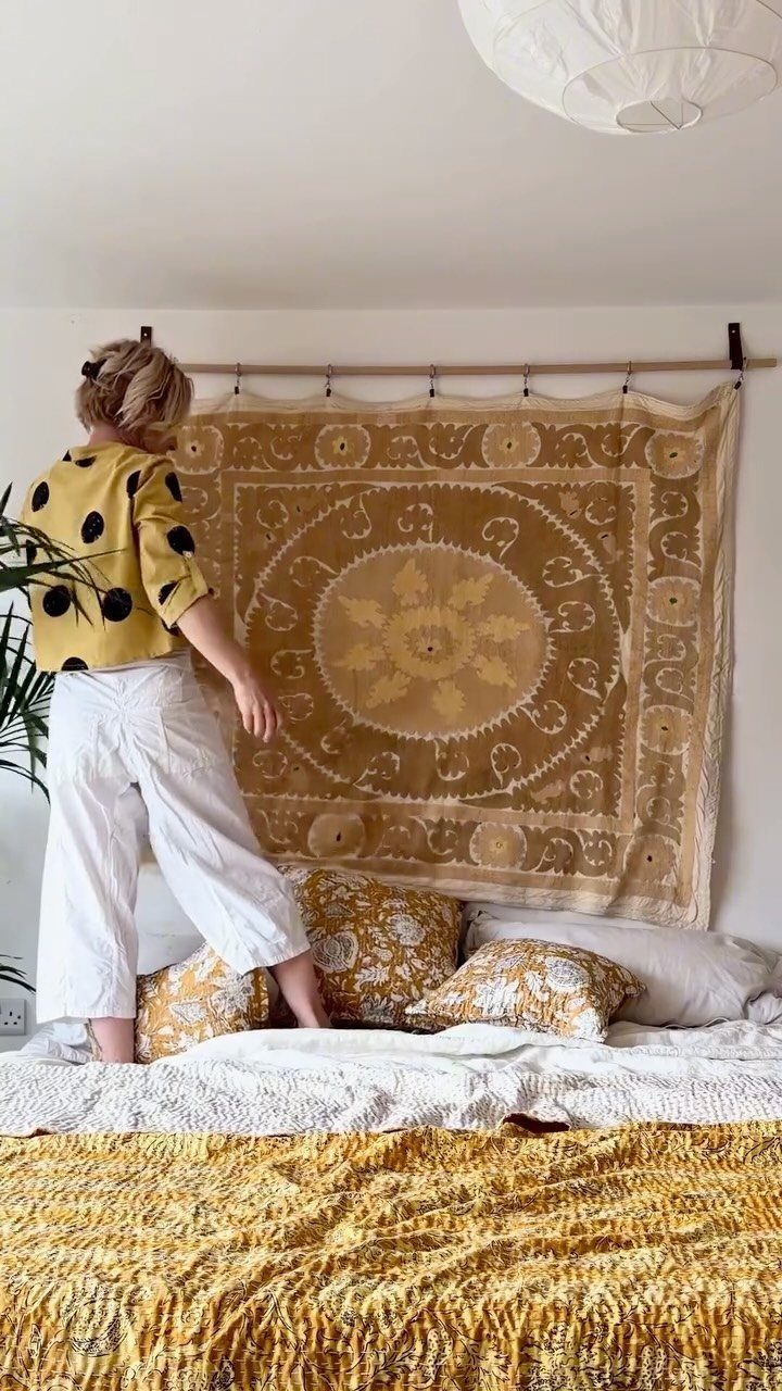 Person adjusting a large patterned fabric wall hanging above a yellow bed