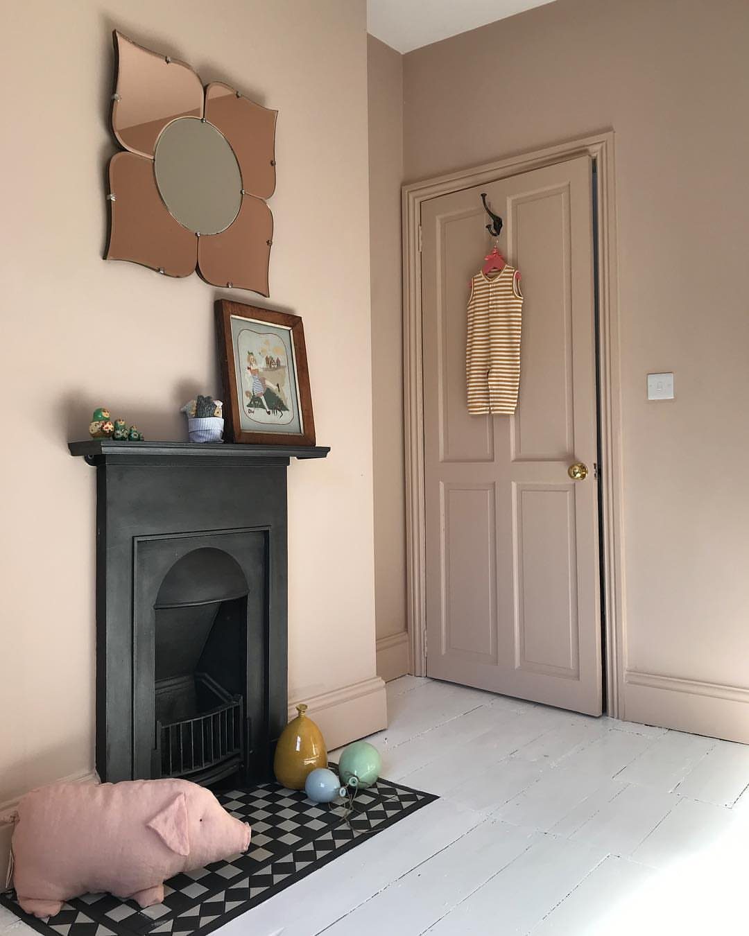 Beige painted walls in a room with a black fireplace and flower mirror.
