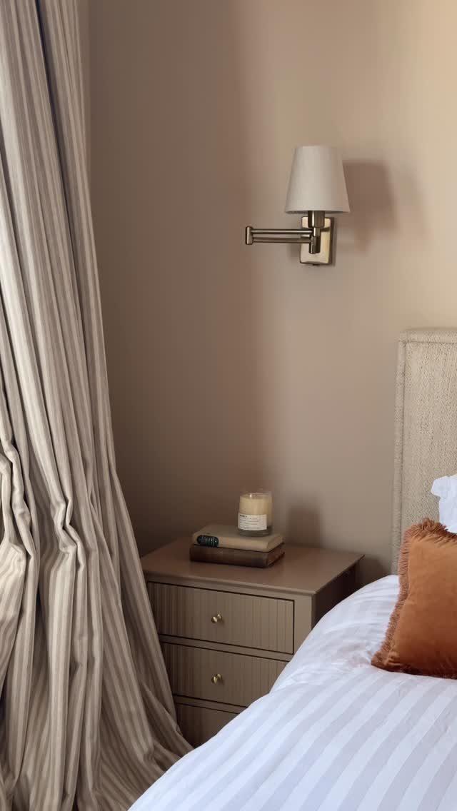 Beige bedroom walls with a matching curtain, nightstand, and white striped bedding.