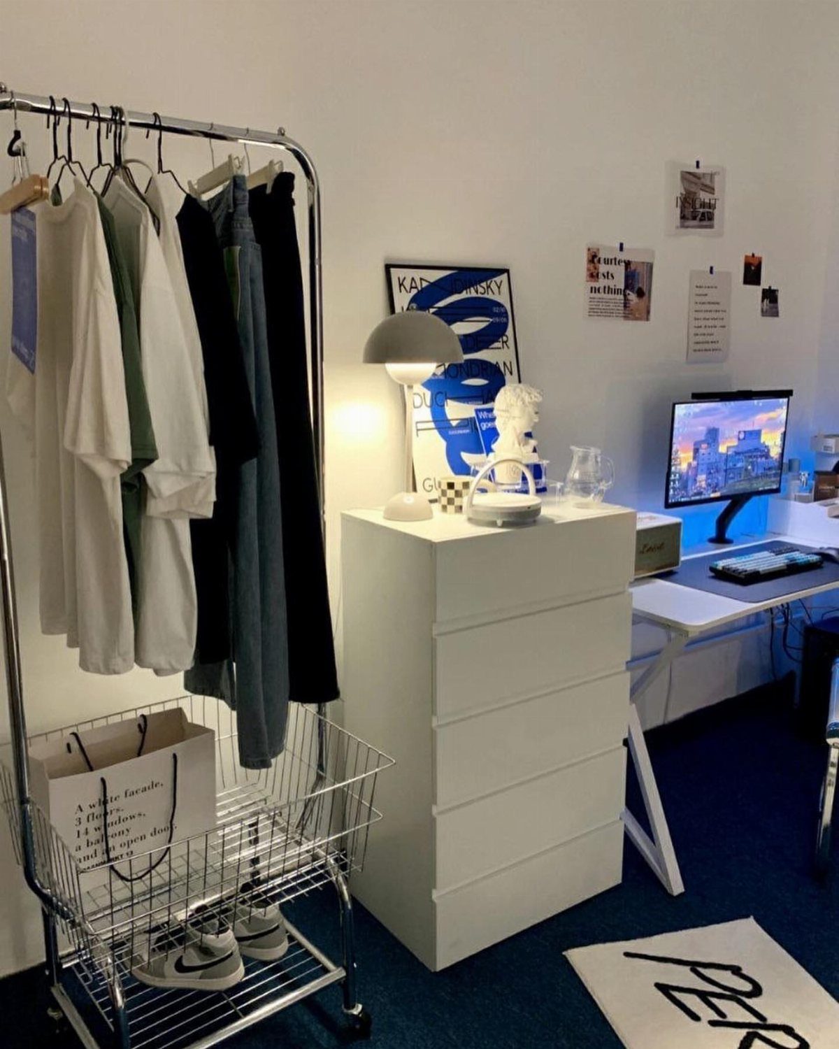 Minimalist white room with clothing rack, white dresser, and a computer desk setup.