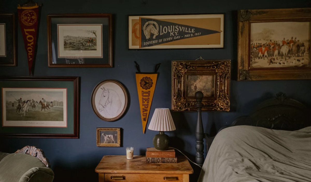 Dark blue bedroom wall with horse racing art, pennants, and a wooden nightstand.