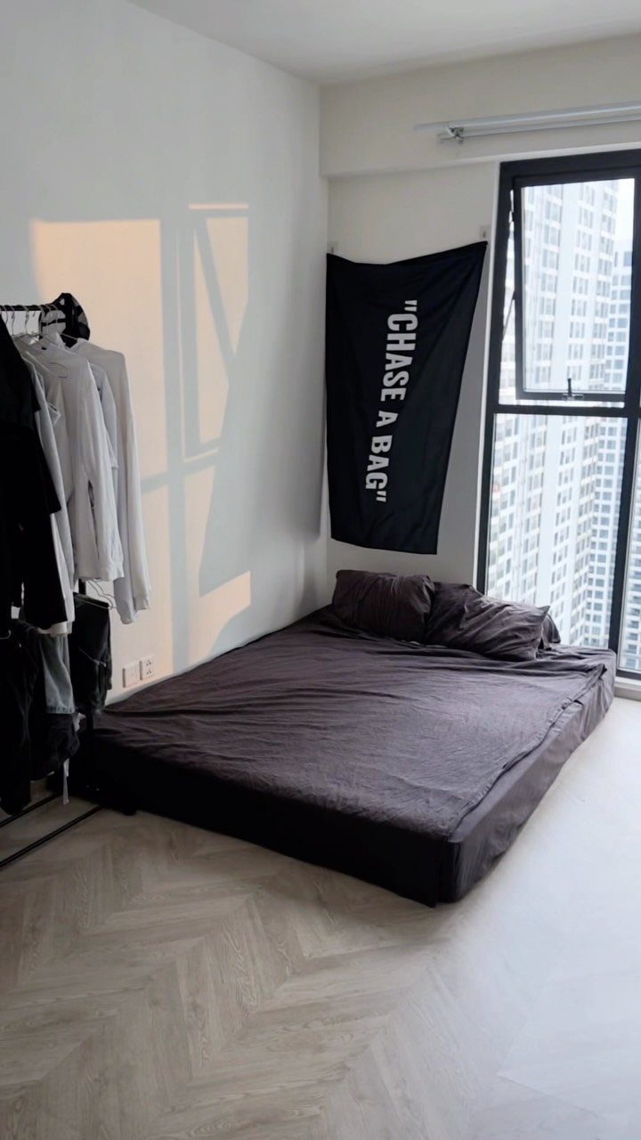 Minimalist bedroom with a low brown bed, clothing rack, and black wall banner.