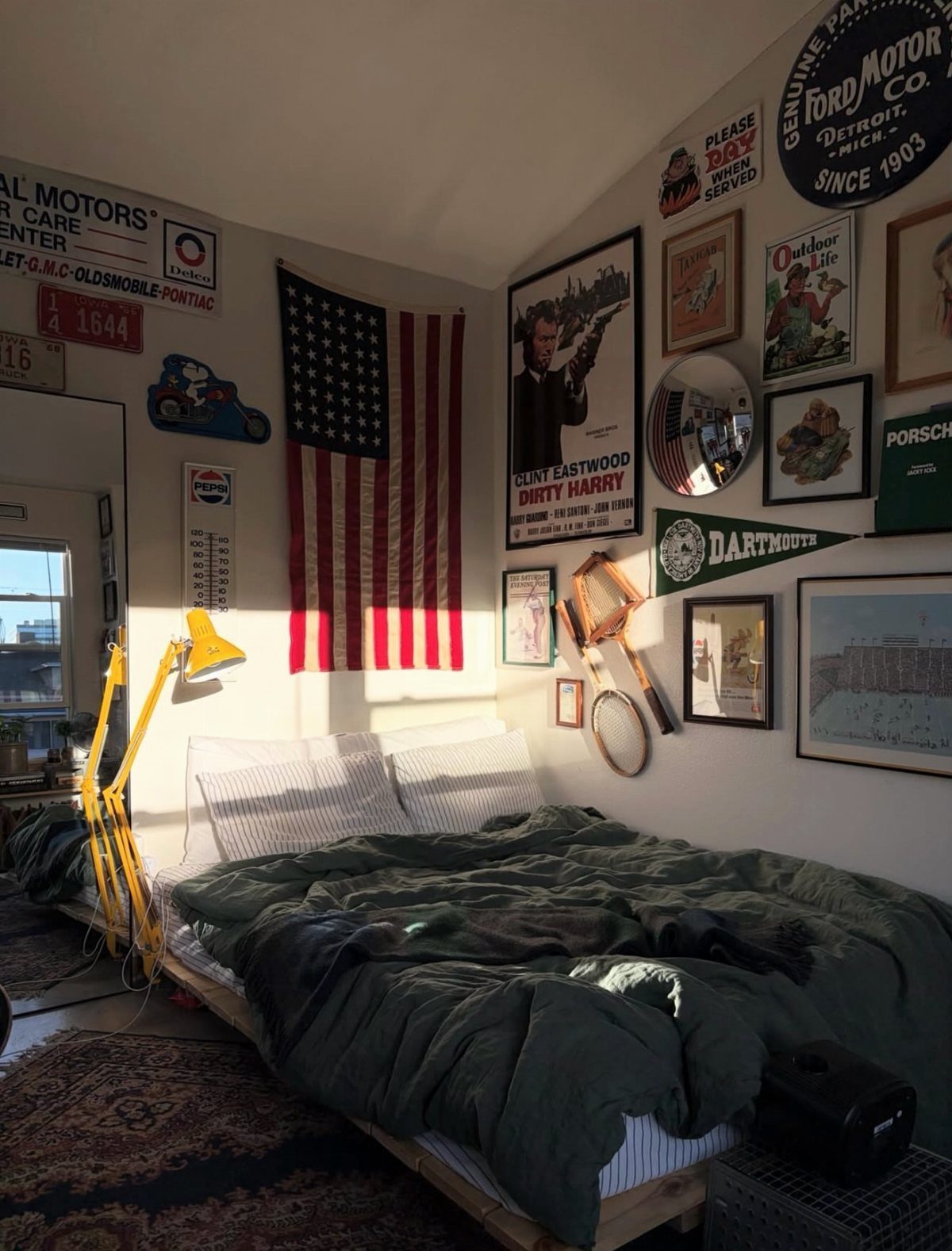 Bedroom with dark green bedding and walls covered in vintage signs and posters.