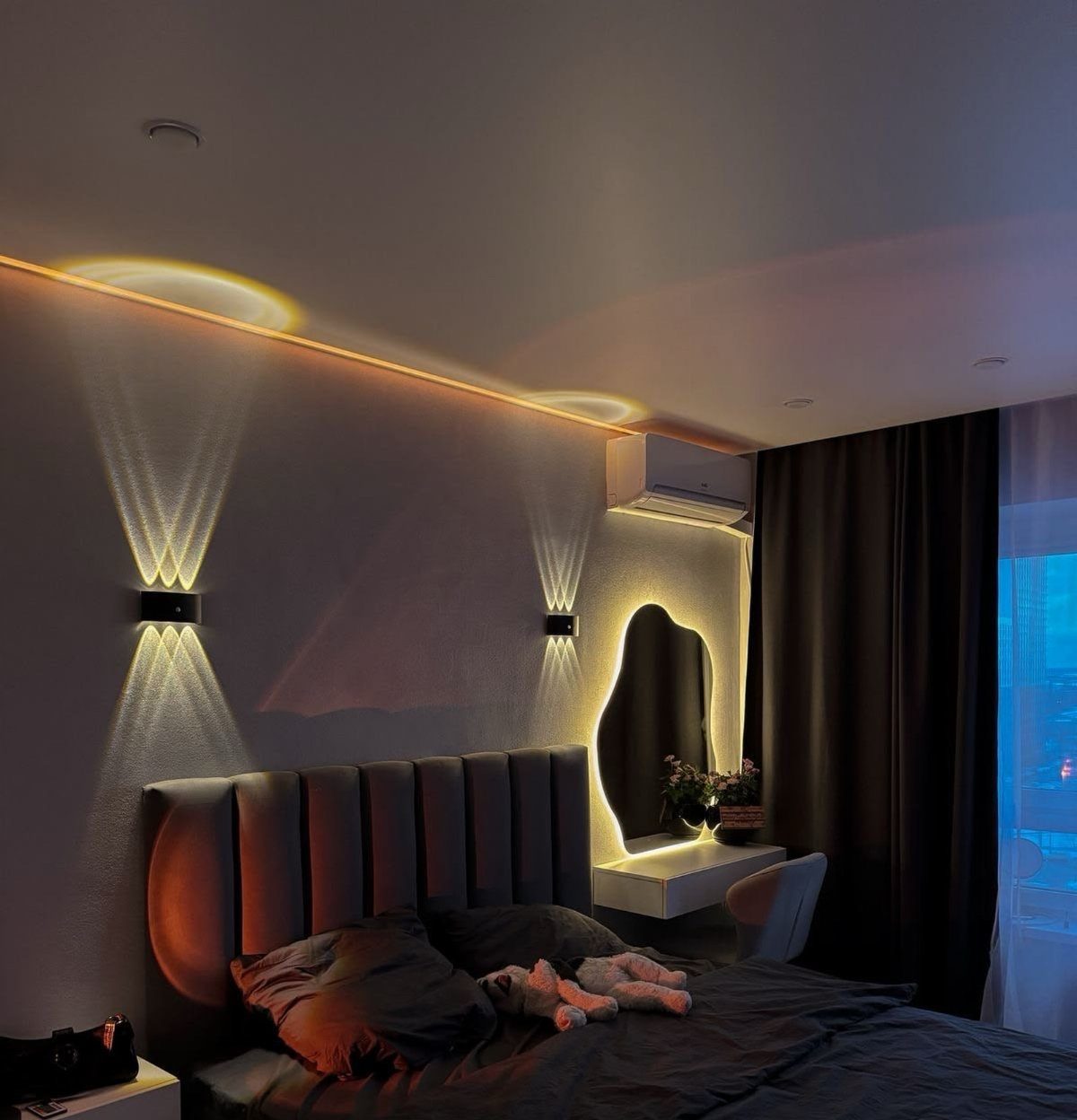 Two black wall-mounted sconces casting light patterns above a grey fluted headboard.