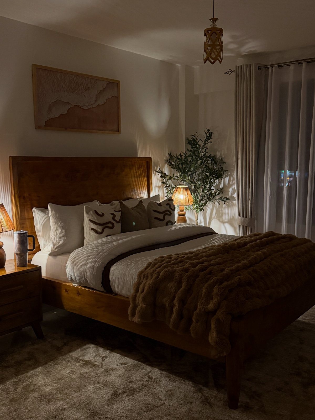 Wooden bed frame with white linens and a green plant in a warm bedroom