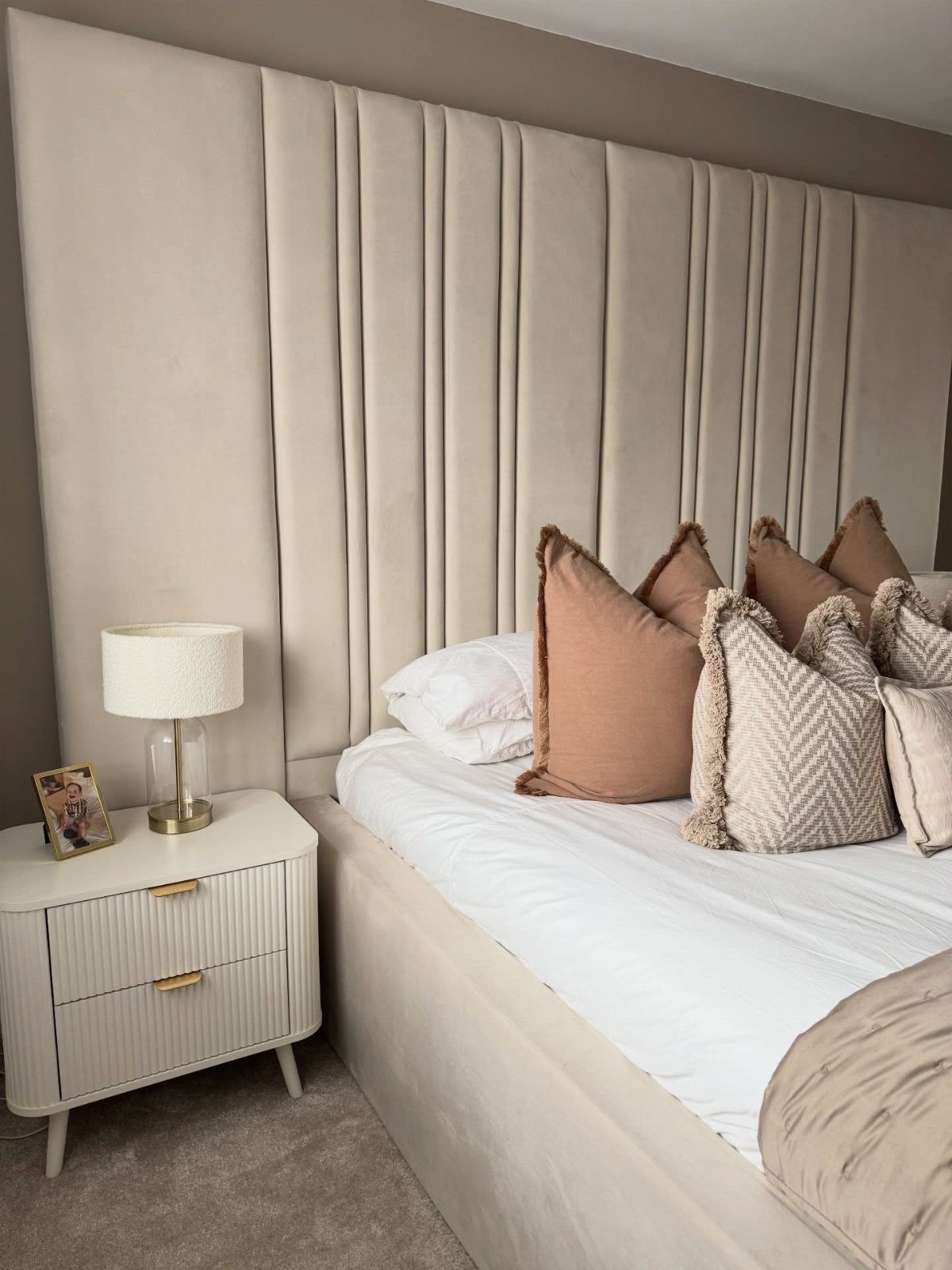 Beige velvet fluted headboard with a white nightstand and brown decorative pillows.