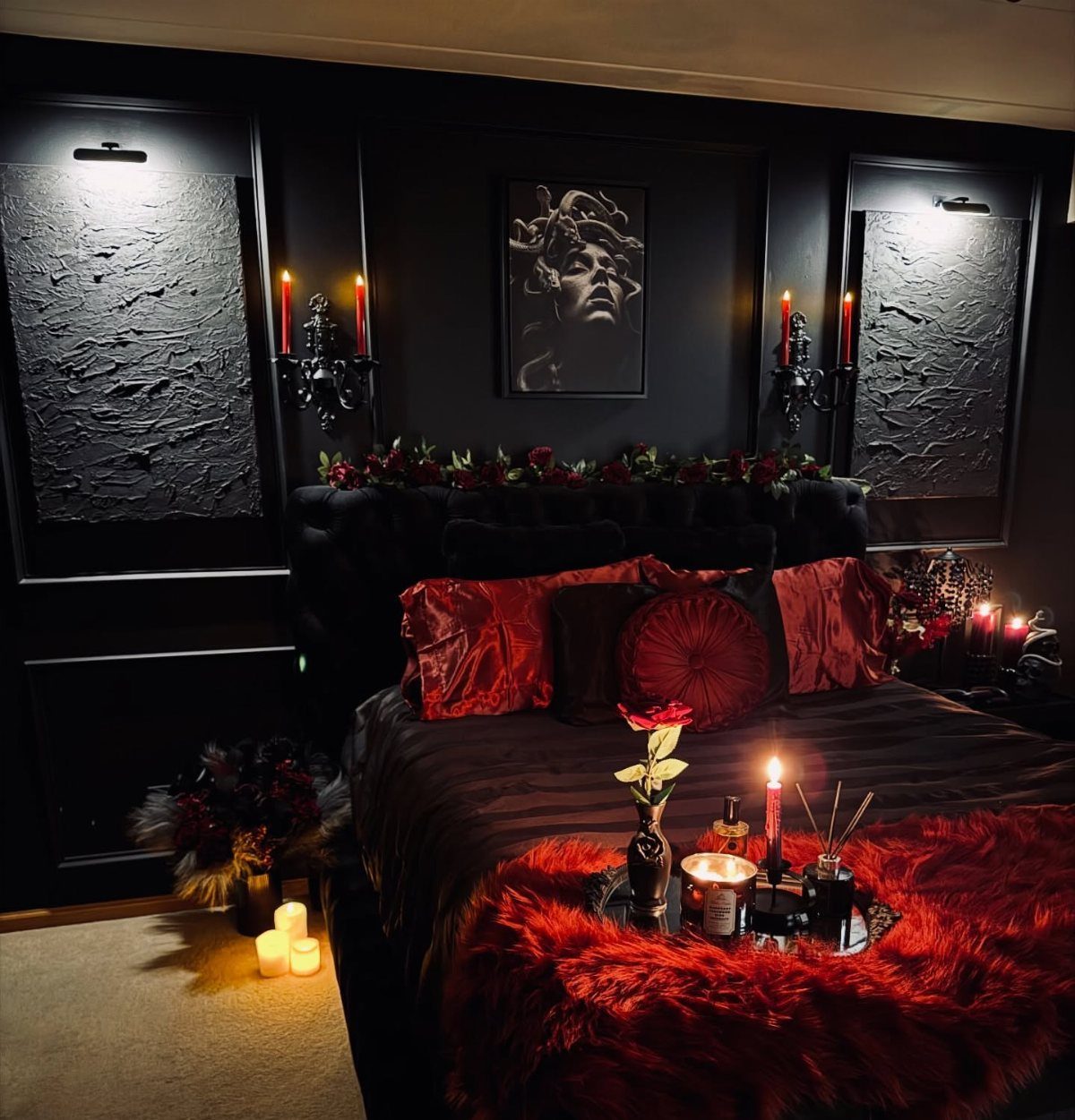 Dark bedroom with black walls, red satin bedding, and glowing red candles.