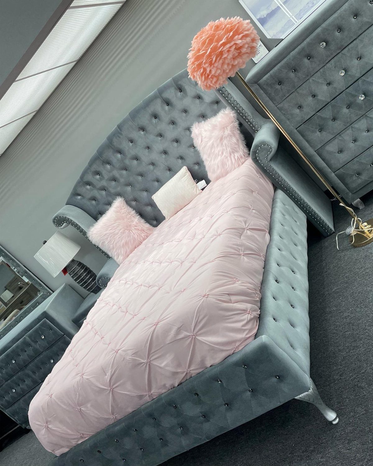 Grey tufted velvet bed with pink bedding and fluffy pink accent pillows.