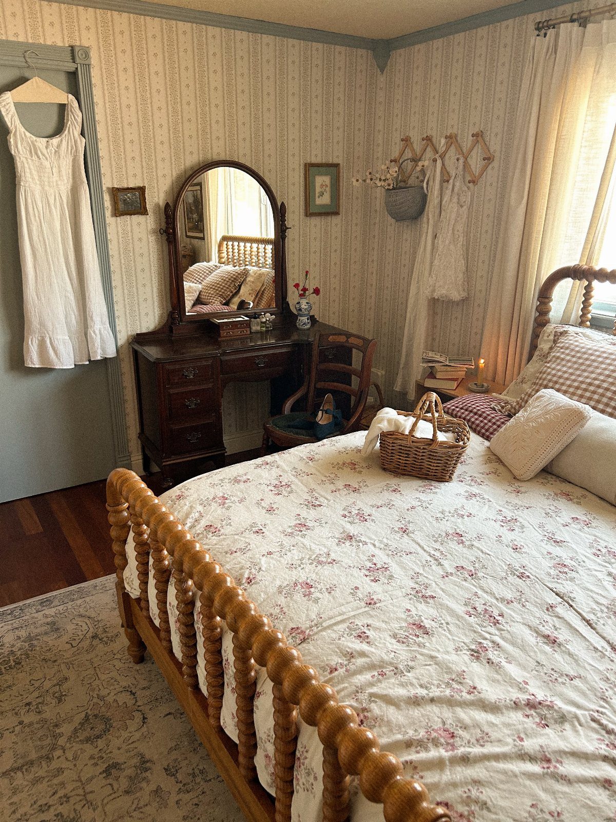 Wooden spindle bed with floral linens and a vintage dark wood vanity mirror.