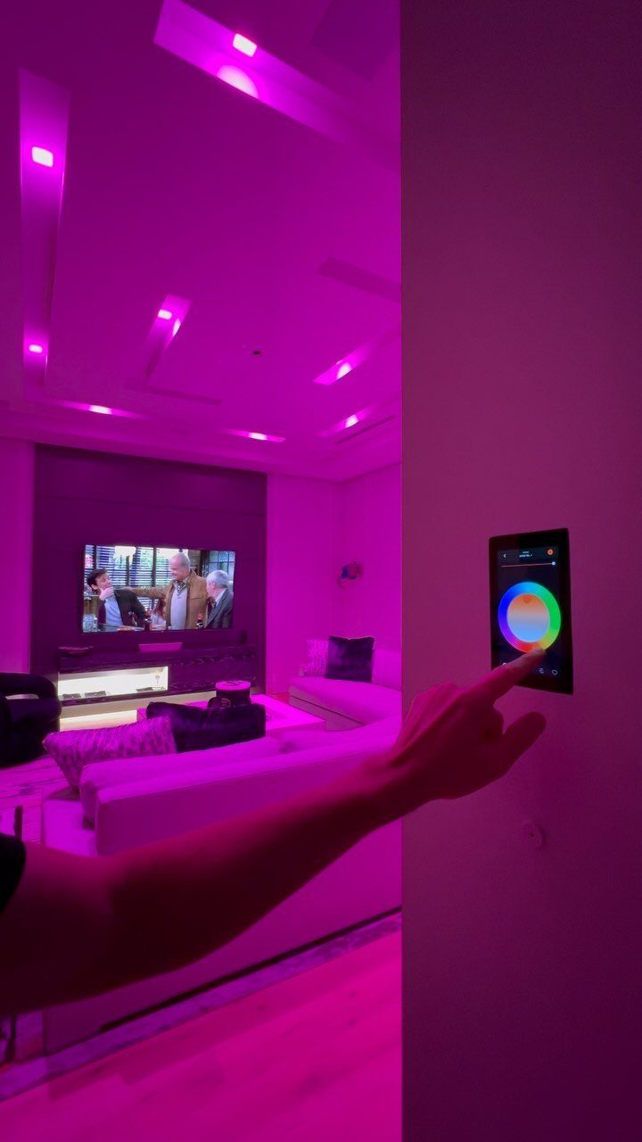Hand adjusting a digital color wheel on a wall panel for purple room lighting.