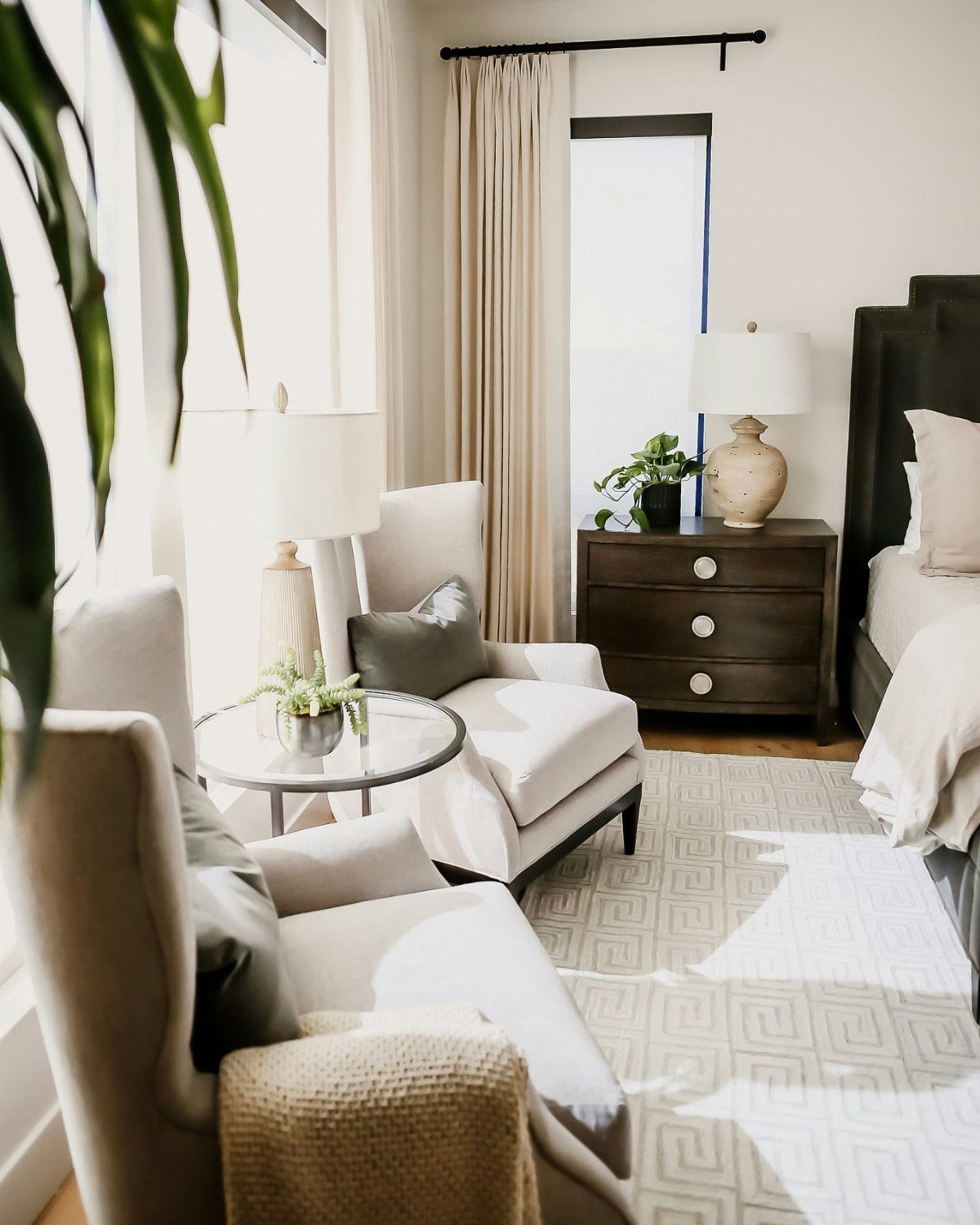 Two cream armchairs and a glass table creating a seating nook in a bedroom.