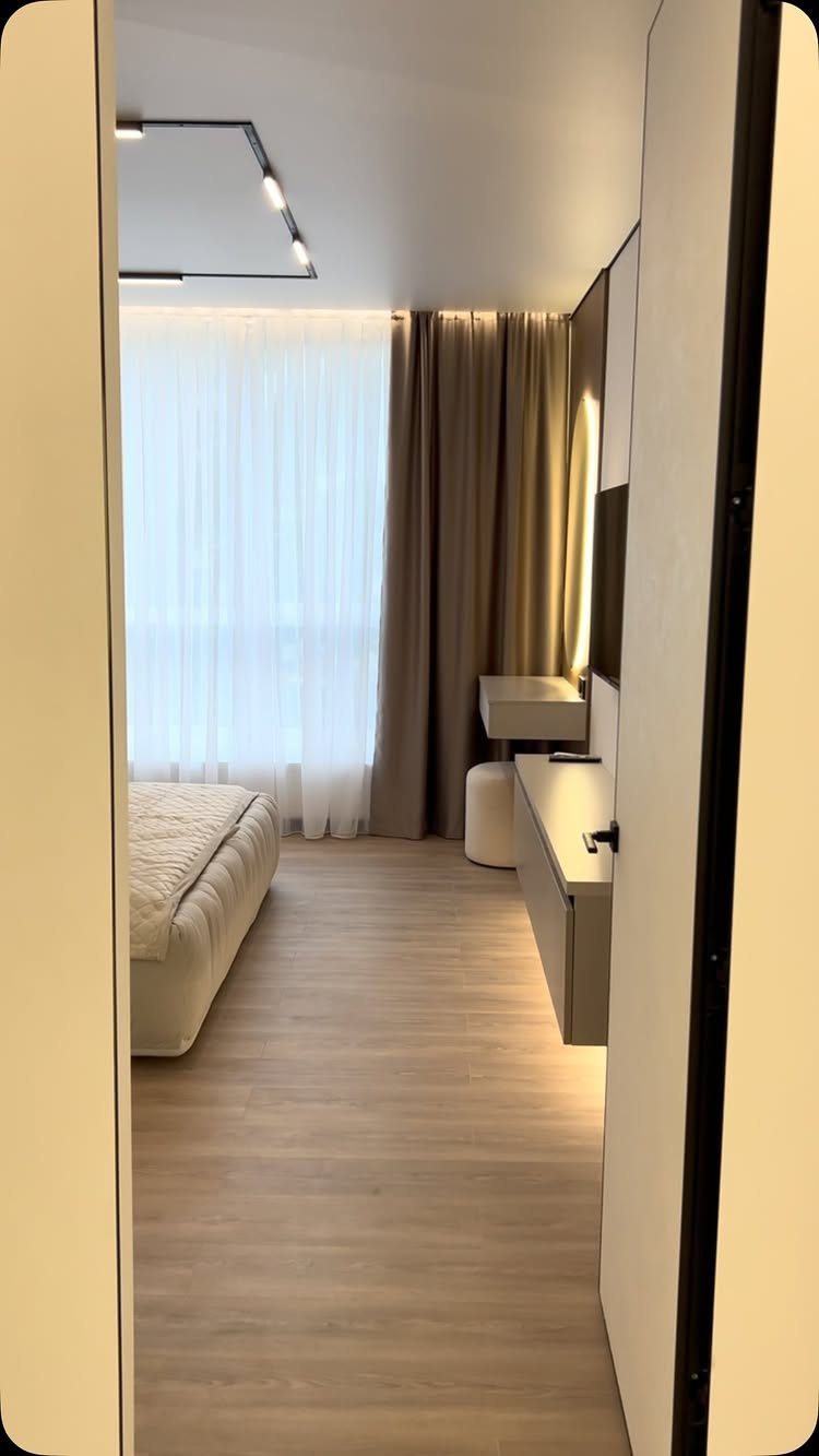 Modern minimalist bedroom with neutral tones, light wood floors, and sleek white furniture.