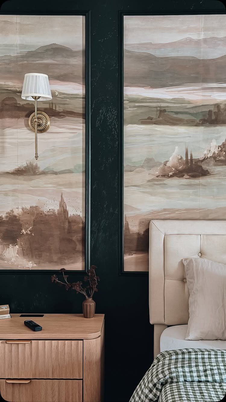 Two large landscape paintings hanging on a dark wall above a tufted headboard.